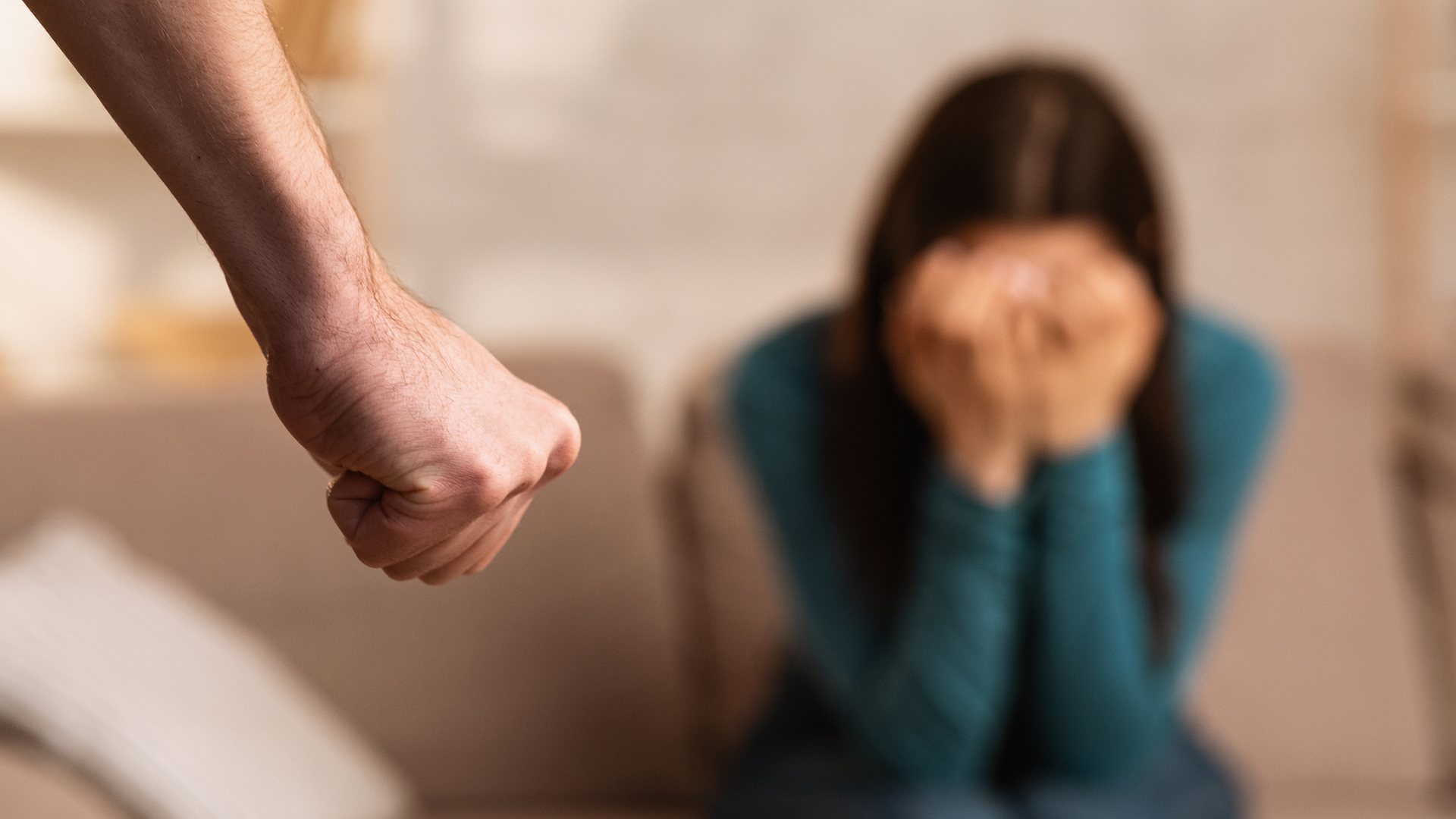 Eine verzweifelte junge Frau mit den Händen vor dem Gesicht. Im Mittelpunkt ist eine geballte Faust.